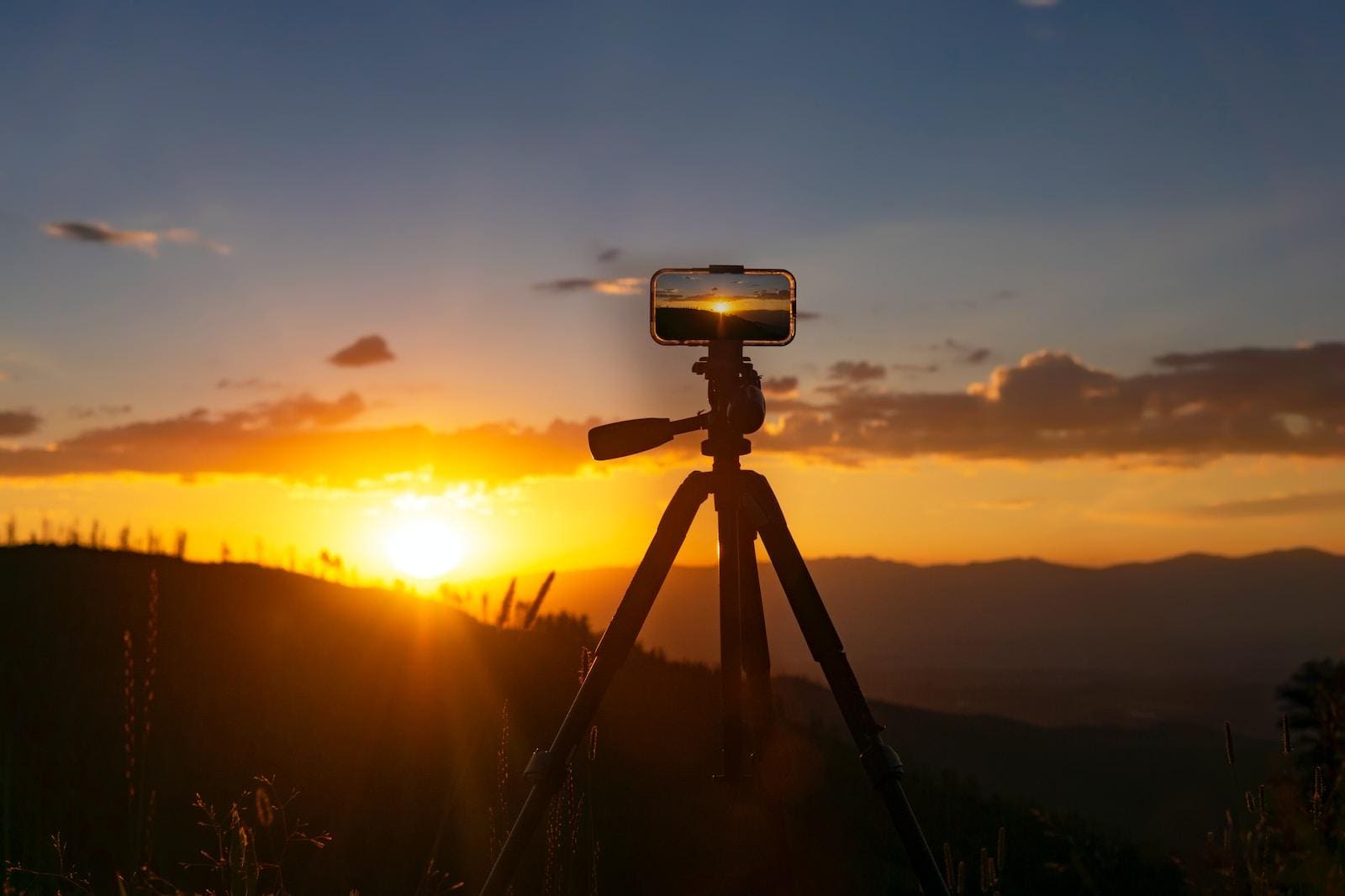 a camera on a tripod with the sun setting in the background